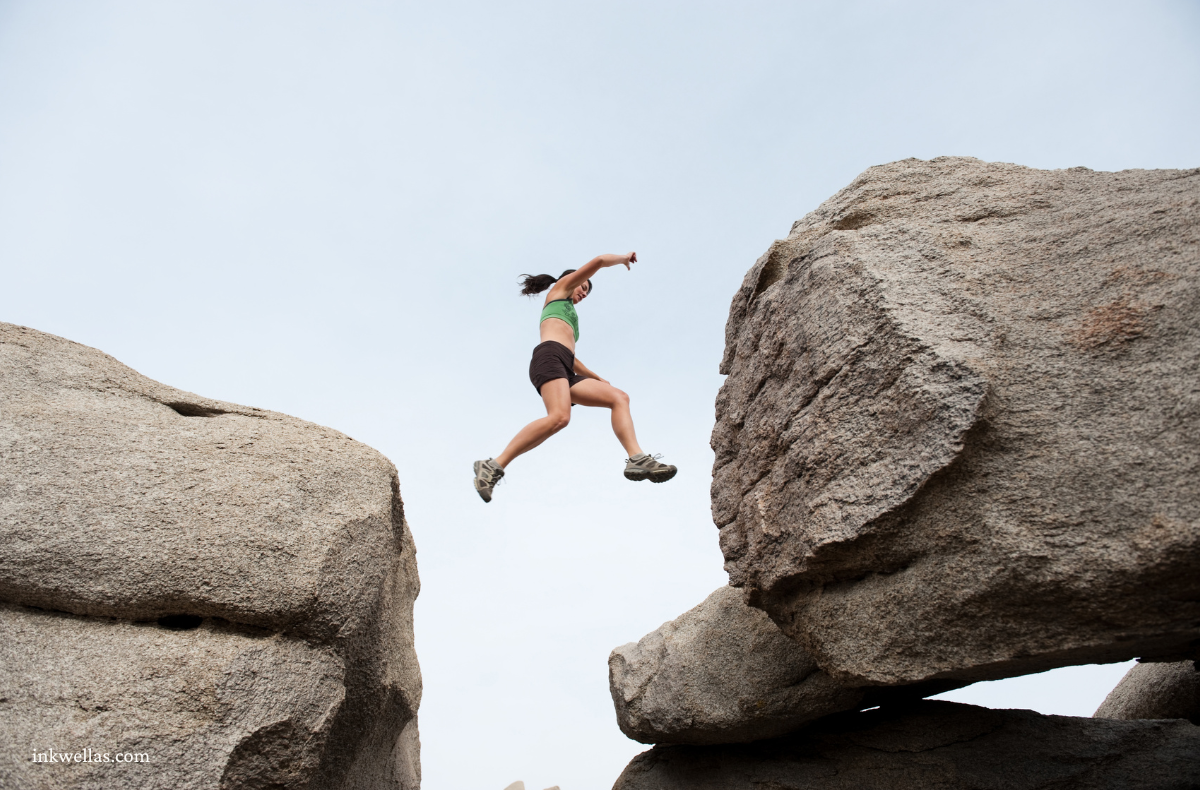 a woman jumping from rock to rock, mid-air in the gap.