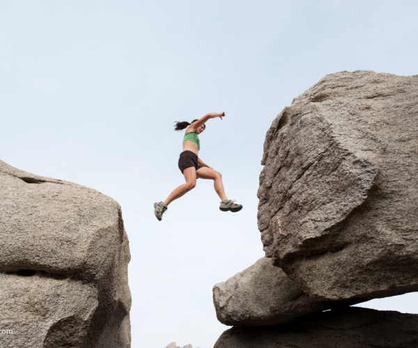 a woman jumping from rock to rock, mid-air in the gap.